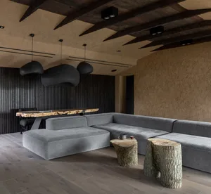 A modern living room featuring a concrete wall, a large corner sofa, and wooden tree stump tables.