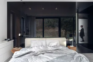 Modern bedroom with minimalist decor, featuring a white bed and natural light from large windows.