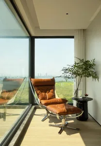 A modern leather and metal chair with a footrest in a living space with large windows.