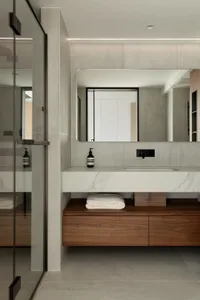 Modern minimalist bathroom with marble countertop and wooden storage, featuring a sleek sink, large mirror, and glass shower 