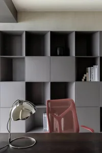 A minimalistic home office with concrete grey shelves, a red mesh office chair, a black desk lamp, and some books.