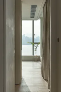 A modern residential hallway featuring white oak wood flooring and a view through the window to the cityscape.