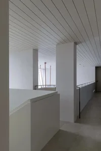Modern, industrial-style corridor with concrete walls, floors, and a minimalist design, featuring a railing with a metal hand