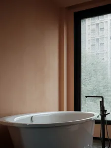 A minimalist bathroom with a white ceramic bathtub and a window with blinds.