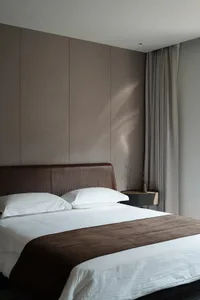 Interior view of a modern minimalist bedroom featuring a brown leather headboard, white linens, and a single brown decorative