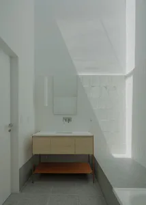 A minimalist bathroom with white ceramic tiles, concrete flooring, and a wood vanity.