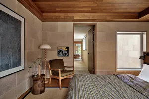 A modern minimalist bedroom featuring stone walls, a wooden floor, and a comfortable bed with a striped blanket.