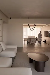 Modern minimalist living room with neutral tones, featuring a large sofa, a round coffee table, and a dining area in the back