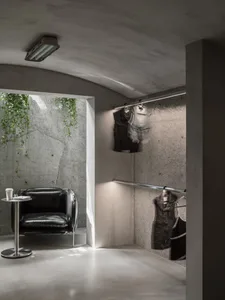 Modern clothing shop with concrete walls, industrial lighting, and minimalist black armchair.