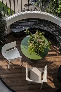 Industrial-style outdoor seating area with wooden floor, marble table, and white chairs with green plant on table.