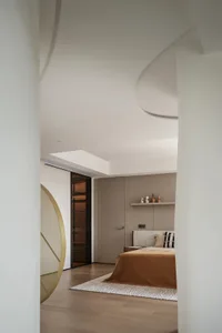 A minimalist bedroom with a beige color scheme and wooden flooring, featuring a bed with a soft bedspread and pillow, and a s