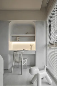 A minimalist home office with white walls, shelves, and furniture, featuring a wooden floor, a white chair, and a vase with d