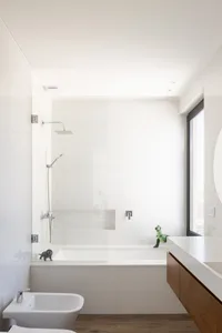 Modern minimalist bathroom with white tiled walls, a glass shower enclosure, a bathtub, and a wooden floor.
