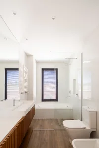 Modern bathroom with white tiled walls, a wooden floor, a glass shower enclosure, a bathtub, a sink, a mirror, and a toilet.