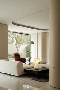A minimalist modern living room with white furniture, a red armchair, and a glass coffee table.