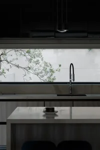 A modern, minimalist kitchen with a marble countertop and a view of greenery outside the window.