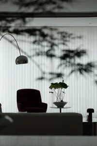 A modern minimalist living room with a glass window, velvet armchair, and potted plant on a side table.