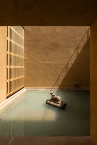 A minimalist spa room with concrete walls, a glass window, and a water feature with a stone sculpture of a dog.