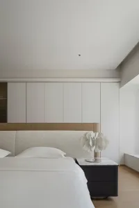A minimalist bedroom with a textured fabric headboard and white bedding.