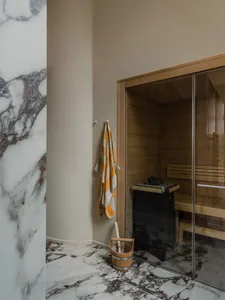 Modern marble sauna room with wooden elements and a glass door.