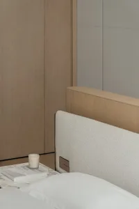 現代簡約臥室，配有白色床鋪、布料軟包床頭板、木質家具，以及一張放有蠟燭的邊桌