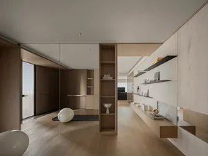 A spacious, minimalist living room with wood flooring, shelves, and furniture.