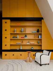 A modern living space featuring a bright yellow bookshelf and a comfortable white armchair.