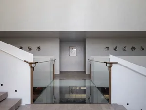 Modern minimalist interior featuring sleek glass walkway, concrete walls, and metal railings.