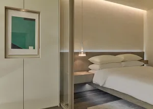 A modern minimalist bedroom with a floating bed, white bedding, and a framed abstract green painting on the wall.