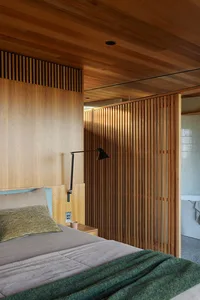 A modern minimalist bedroom featuring a bed with wood-paneled walls, a green blanket, and a black adjustable lamp attached to