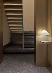 A modern staircase features concrete steps illuminated by a sleek, angular lamp with a triangular shade.