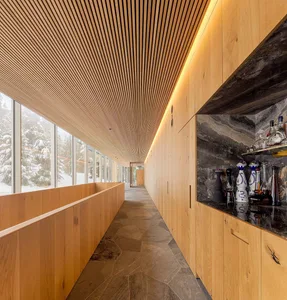 Modern interior corridor with wooden walls and ceiling, featuring a bar area with black marble countertops and assorted bottl
