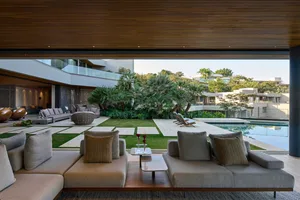Modern living room with outdoor space featuring a comfortable couch, coffee table, and poolside area with plants and lounge c