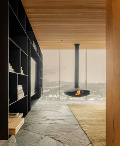 Modern minimalist living room with suspended fireplace and floor-to-ceiling windows overlooking snowy landscape.