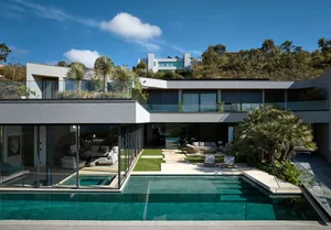 Modern modernist high-rise home with glass walls, concrete balconies, and lush greenery on a hillside.