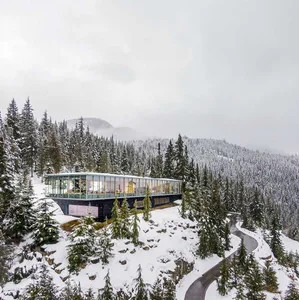 A modern house nestled on a snow-covered mountainside with glass walls and a concrete structure.