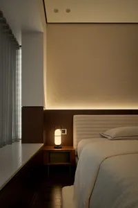 Modern bedroom with a textured beige wall covering, a white bed, and a lamp on a side table.