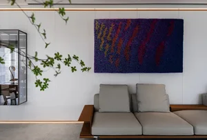 Modern living room featuring a sofa, abstract art hanging on the wall, and a view into an office space with a glass door.