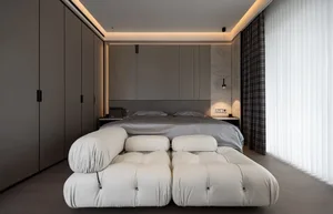A modern minimalist bedroom featuring a large bed with a tufted headboard, a white fabric bench, a large window with vertical