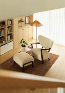 A cozy living room with a comfortable armchair and matching ottoman, wooden flooring, and a side table with a plant and books