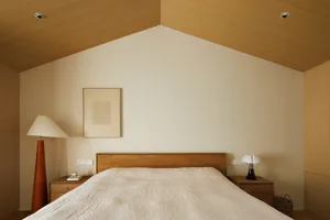 A minimalist bedroom with a wooden headboard, cotton blanket, and white walls.