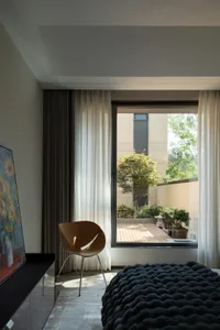 Modern bedroom with glass window overlooking outdoor terrace adorned with green plants and trees.