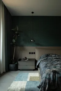 A modern bedroom featuring a bed with a mixed-material headboard, patterned bedding, and a side table with a single drawer. A