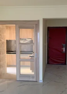 Modern entrance with wooden glass-paneled door, beige walls, and open space beyond showing kitchen.