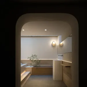 A minimalist bathroom with wooden accents and concrete elements, featuring a tub, sink, and wall-mounted lights.