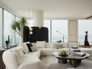 Modern living room with a white fabric couch, minimalistic design, and large windows overlooking a cityscape.