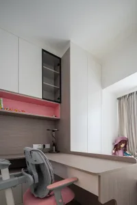 A modern study room with a wooden desk, grey chair, and white and pink cabinets.