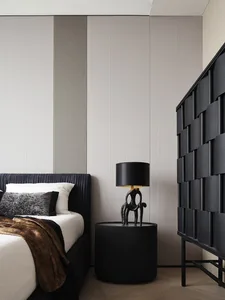 A modern minimalist bedroom featuring sleek, black furniture, a bed with a textured headboard, and a black lamp with a black 