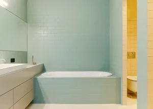 A modern bathroom with a blue-tiled bathtub and white sink.