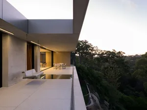 Modern residential exterior with concrete structure, glass walls, and metal accents.